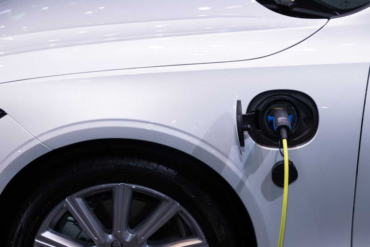 Weißes Auto an einer Ladesäule, ein gelbes Ladekabel steckt in der geöffneten Ladeklappe über dem Vorderrad