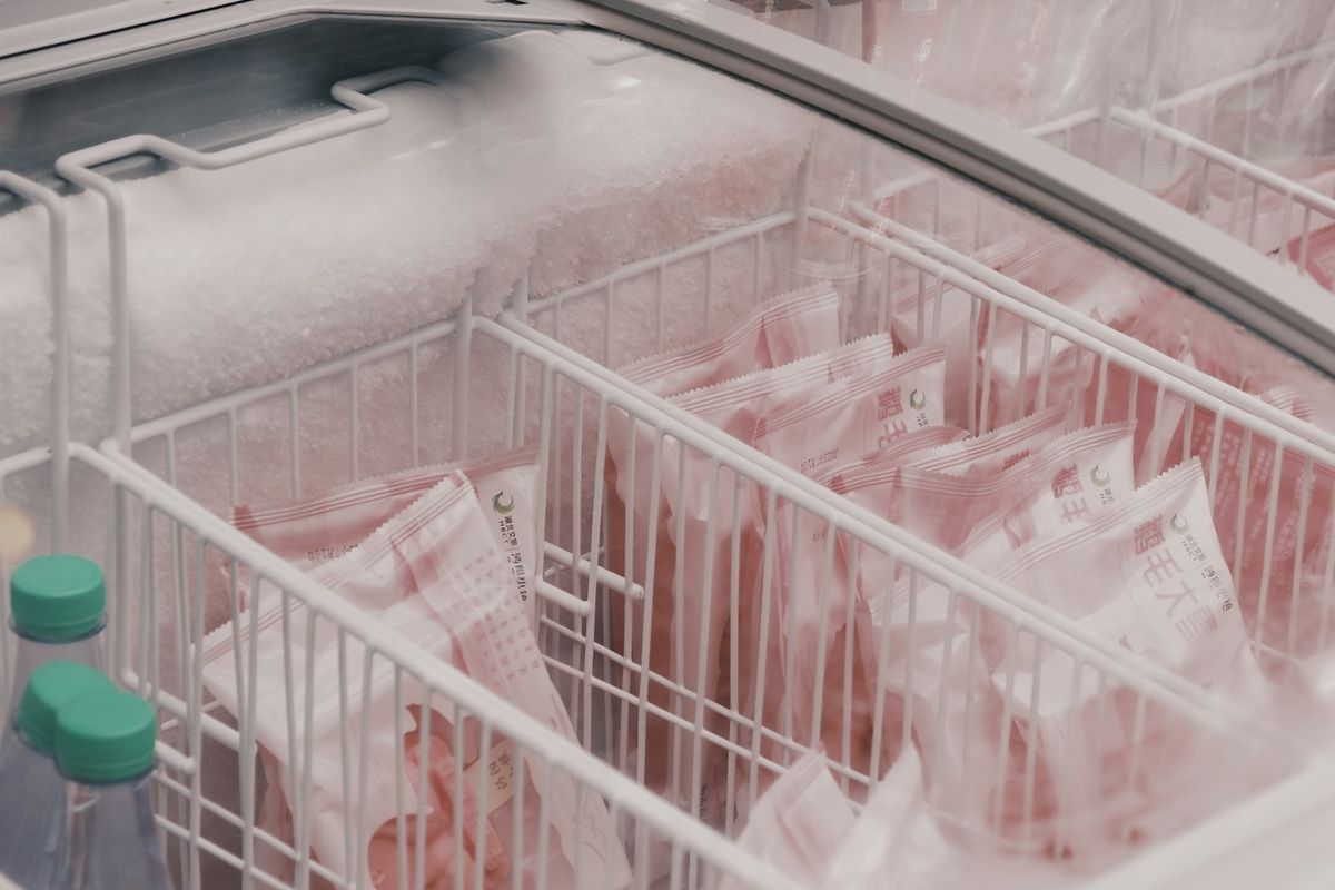 Offene Gefriertruhe mit vereistem Rand, in den Drahtkörben liegen verpackte Tiefkühlware