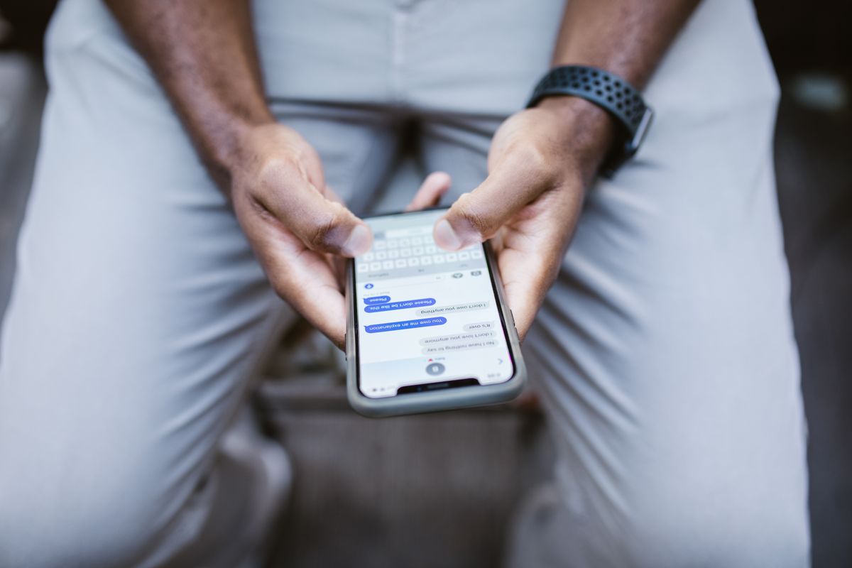 Mann in heller Hose tippt mit beiden Daumen auf einem Smartphone, auf dem ein Chatverlauf geöffnet ist