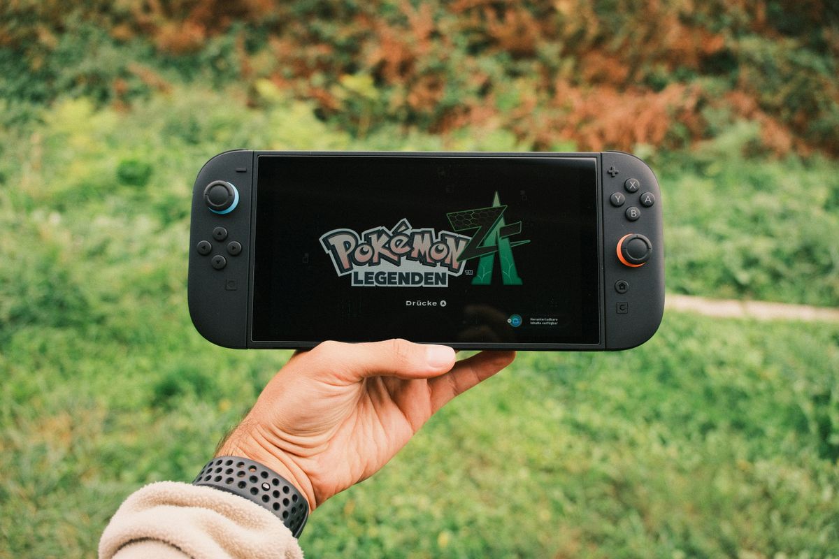 Hand hält eine schwarze Nintendo Switch 2 im Freien, auf dem Bildschirm der Startbildschirm eines Pokémon-Spiels