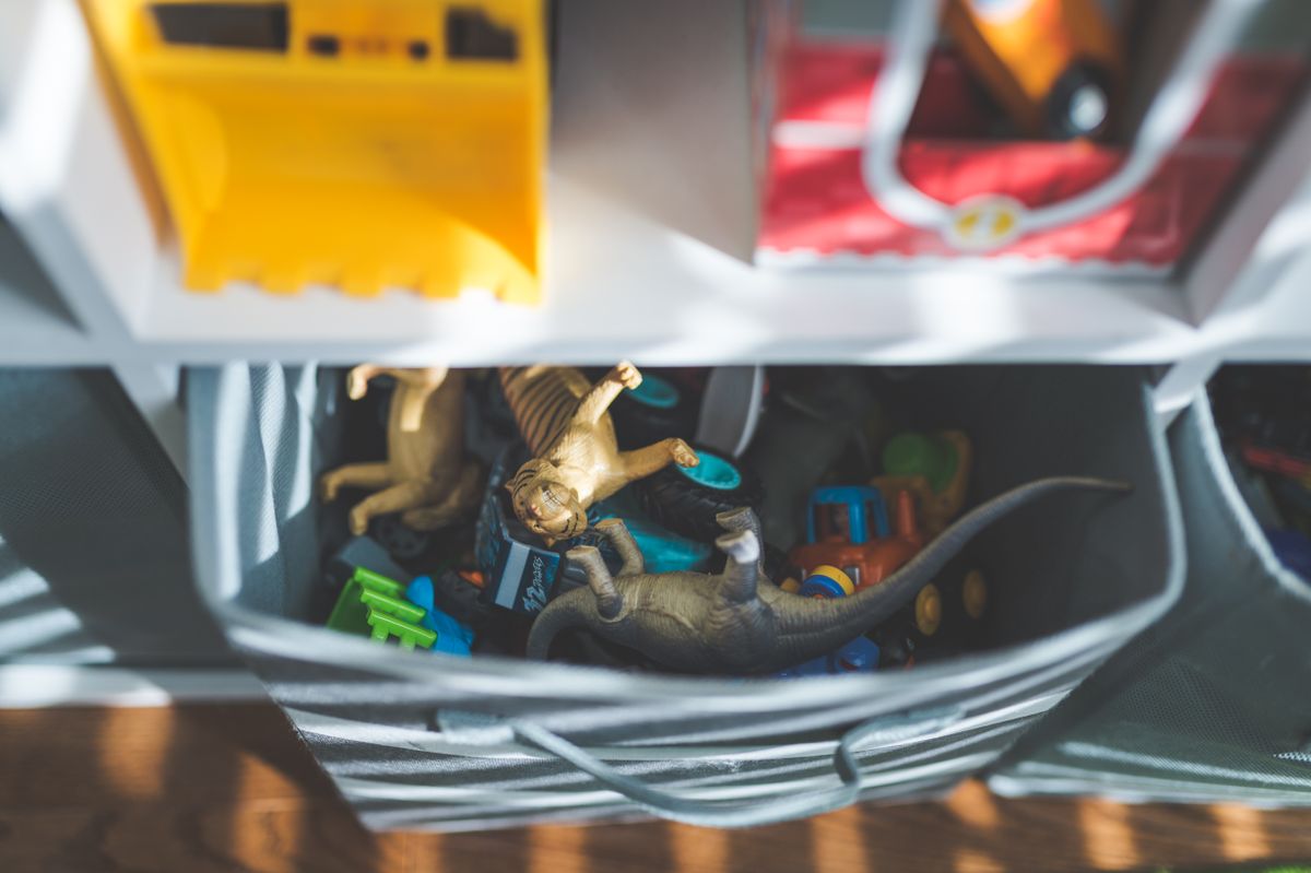 Plastikfiguren und Spielzeugautos liegen in einer Stoffbox unter einem Regalboden