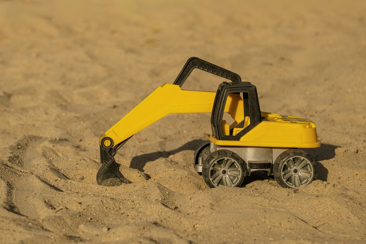 Gelber Spielzeugbagger aus Kunststoff steht mit abgesenkter Schaufel im Sand